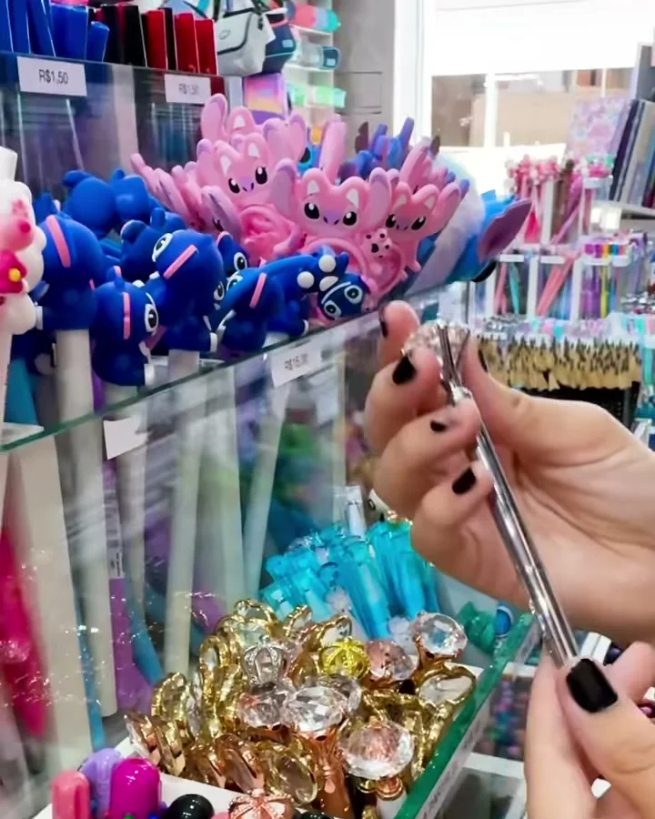 Balcão de vidro com potes de canetas decoradas e a parede de canetas ao fundo