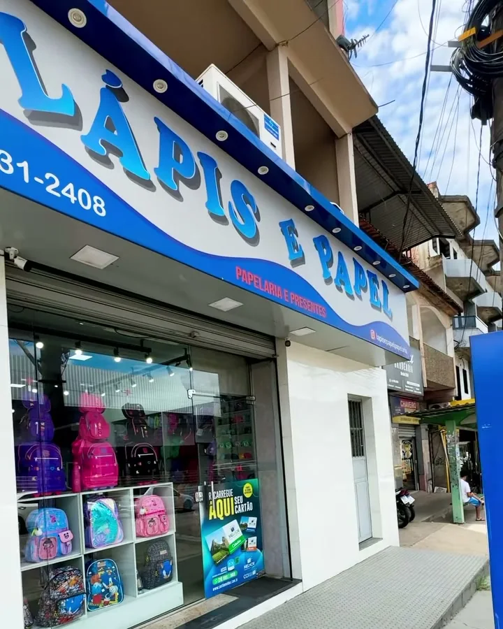 Fachada da Papelaria Lápis & Papel: placa azul com as letras brancas Lápis e Papel, o WhatsApp da loja e a vitrine com mochilas coloridas